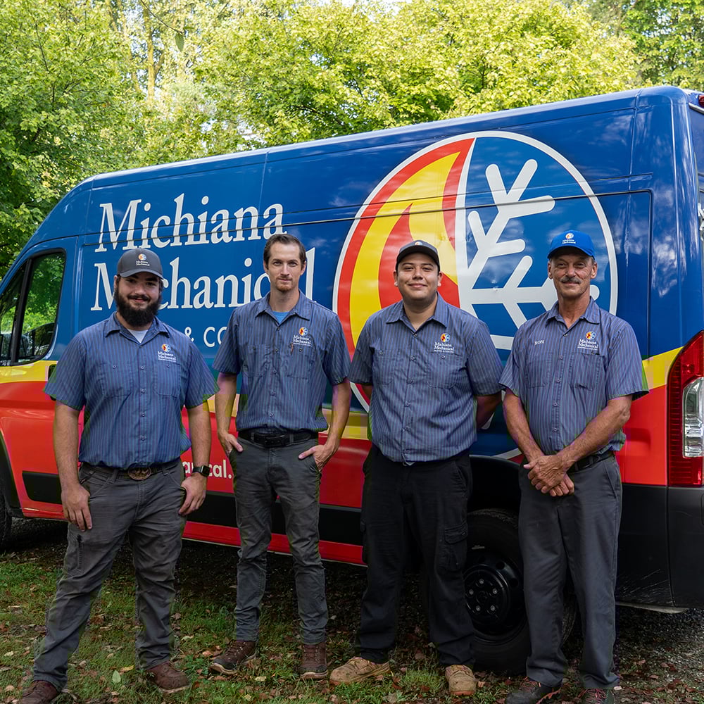 Four HVAC technicians standing in front of a Michiana Mechanical service van