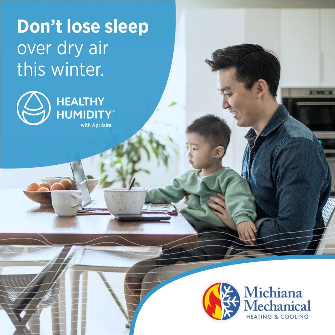 Father working on laptop while holding child at kitchen table with “Don’t lose sleep over dry air this winter” message from Michiana Mechanical